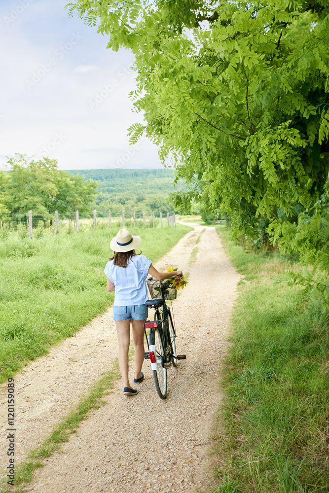 Relaxing in the nature. Rear view shot of a young woman pushing her bike at rural scene. Relaxing in the nature. Rear view shot of a young woman pushing her bike at rural scene.