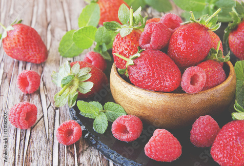 ripe red raspberries and strawberries in wooden bowl  selective focus