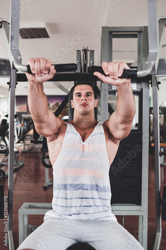 Young attractive adult man exercising and doing weight lifting at fitness gym. Sport training indoors.