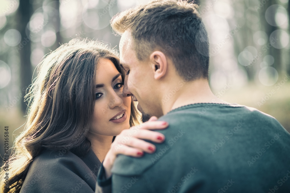 Beautiful young adult couple hugging and kissing. They enjoy autumn nature outdoors. Natural light and warm sunlight.