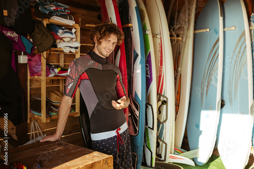 Photography Man in swimsuit using smartphone while standing in surf shack