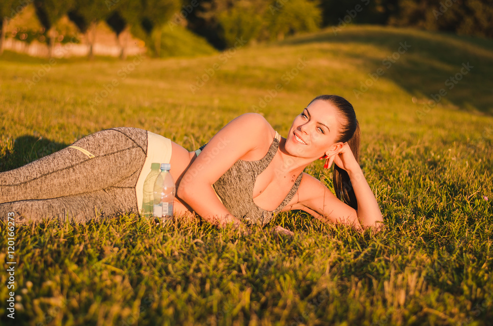 Attractive fitness woman in sportswear lies on the grass in the Attractive fitness woman in sportswear lies on the grass in the