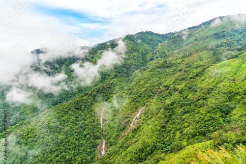 Small waterfall on green mountain ridge in rain forest on cloudy