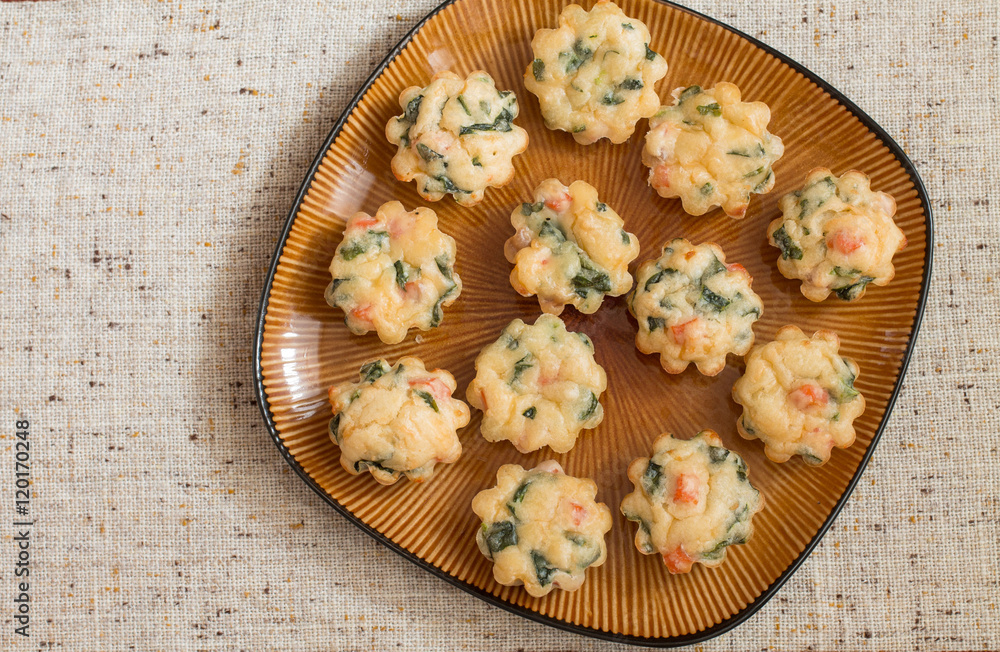 Muffins with salmon, spinach and cheese a big brown plate on tablecloth. Aerial view.