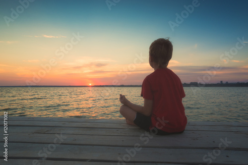 Young boy meditating on a pier