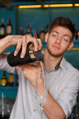 Young handsome barman pouring cocktail drink into glass