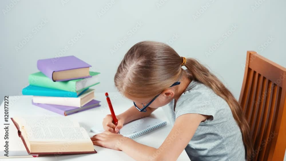 Portrait student girl child 7-8 years old in glasses something writing in her notebook and looking at camera. Top view Portrait student girl child 7-8 years old in glasses something writing in her notebook and looking at camera. Top view