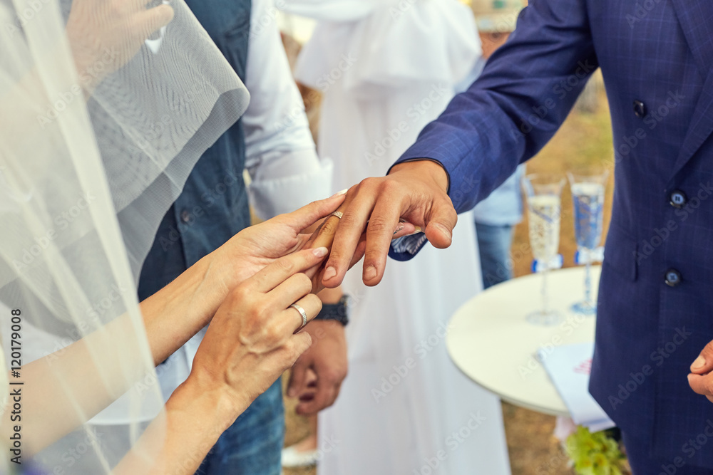 Fototapeta premium Bride putting a wedding ring on grooms finger. Beautiful place for outside wedding ceremony in wood.