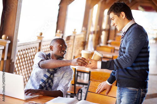 Young man giving coffee cup to his friend in cafe