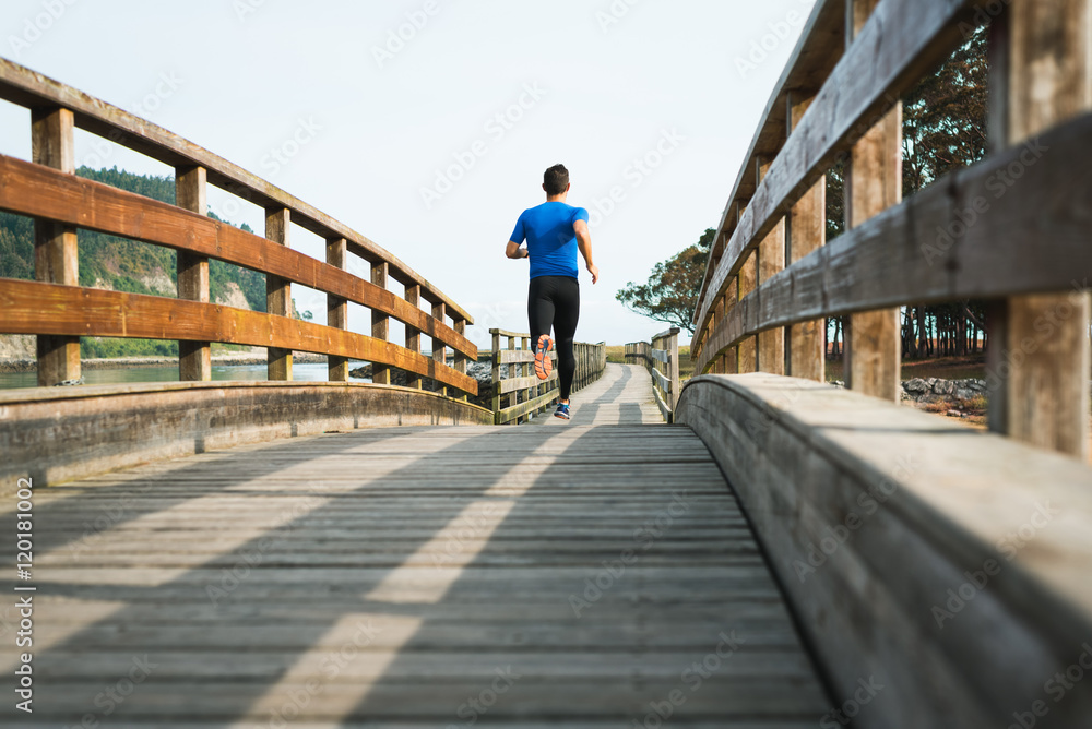 man running in park on wooden walkway training and exercising for trail run marathon race. Fitness healthy lifestyle concept with male athlete outdoor runner.