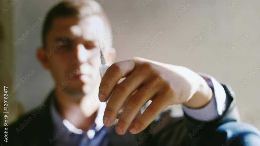 A young man holding a syringe with a drug. Concept: the willpower to quit drugs, danger, crime A young man holding a syringe with a drug. Concept: the willpower to quit drugs, danger, crime