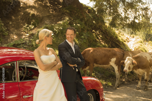 Bridal couple with vintage car waiting on a dirt track