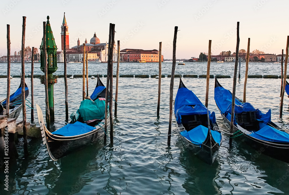 The gondolas  docked at the pier the Piazza San Marco in Venice, Italy at sunset. In the background is Church of San Giorgio Maggiore.    
