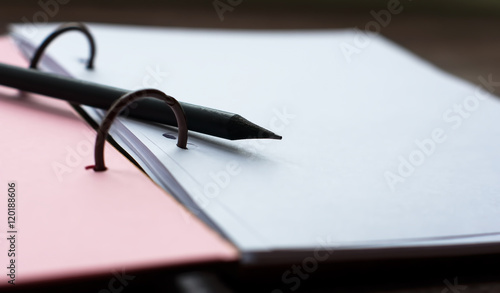 Open notebook with pink pages and a black pencil lying diagonally