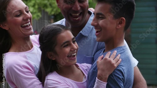 Slowmo video of a mother and daughter embracing the father and son of the family outdoors in a group hug.