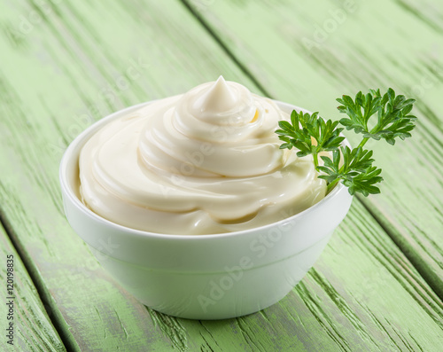Natural mayonnaise in the white bowl on the wooden table.