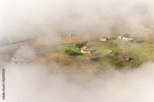 Amazing scenery of idyllic countryside with rolling hills veiled in morning fog. Aerial view of a hilltop farmhouse on a foggy spring morning © Dmytro Kosmenko