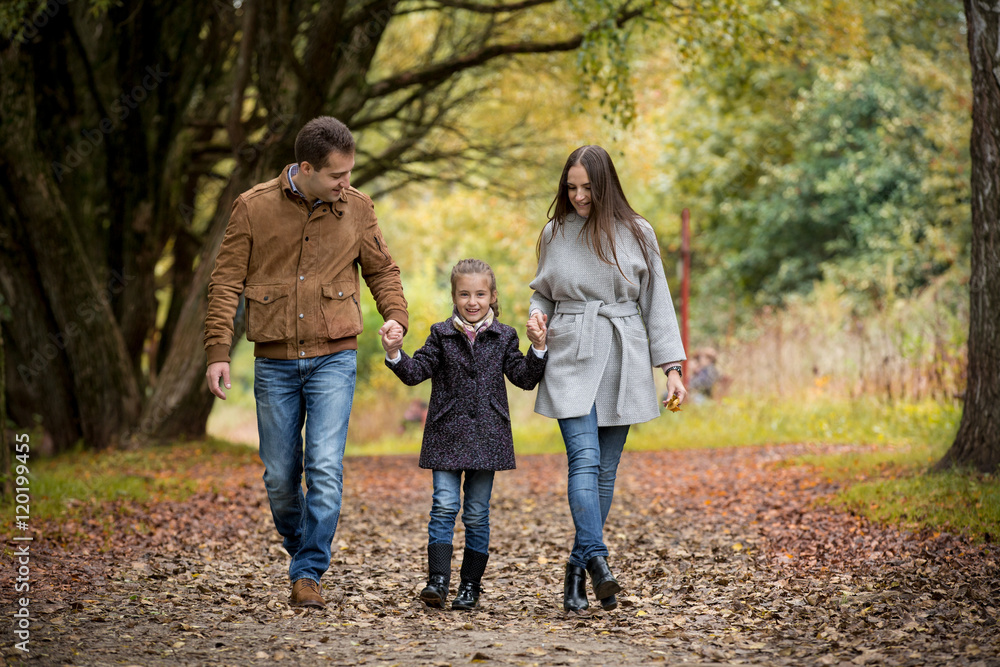 Lovely family walking in the autumn forest. Happy parents enjoying fresh air and beautiful nature, holding hands, talking, smiling and laughing. Healthy lifestyle