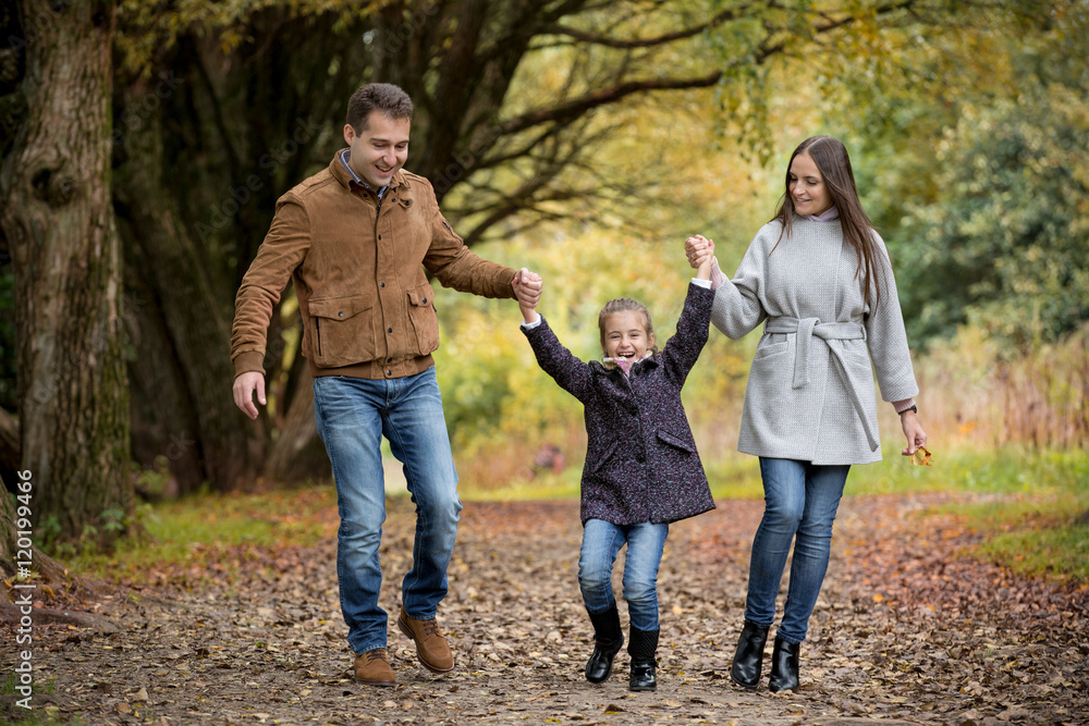Lovely family walking in the autumn forest. Happy parents enjoying fresh air and beautiful nature, holding hands, jumping and having fun. Talking, smiling and laughing. Healthy lifestyle Lovely family walking in the autumn forest. Happy parents enjoying fresh air and beautiful nature, holding hands, jumping and having fun. Talking, smiling and laughing. Healthy lifestyle