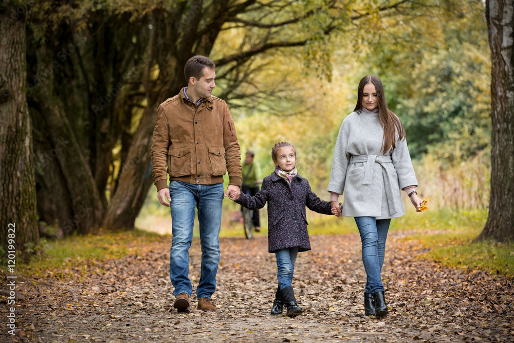 Lovely family walking in the autumn forest. Happy parents enjoying fresh air and beautiful nature, holding hands, talking, smiling and laughing. Healthy lifestyle