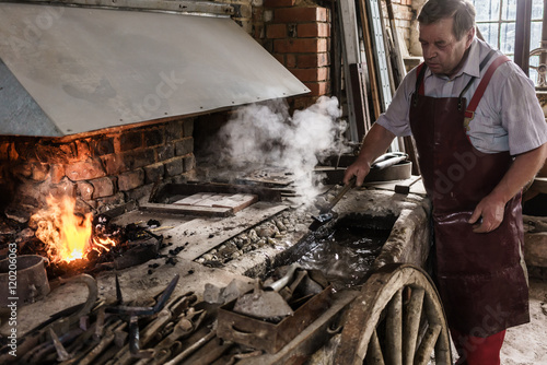 Blacksmith cooling work piece in water front of furnace fire photo