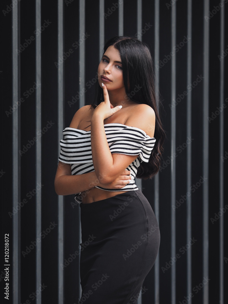 Portrait of young beautiful curvy woman plus size in striped top and black skirt over vertical striped background Portrait of young beautiful curvy woman plus size in striped top and black skirt over vertical striped background
