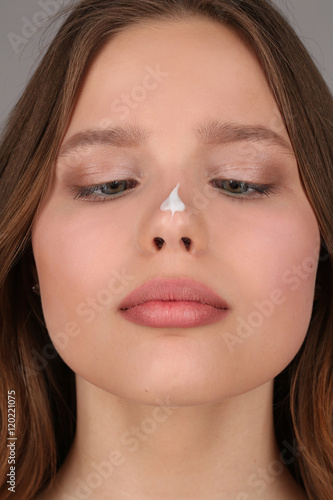 Girl with cream on her nose. Close up. Gray background