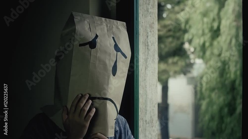 A sad breadbag face crying near a window on a rainy day. Close-up shot.
