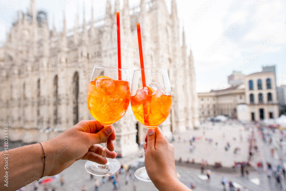 Fototapeta premium Clinking glasses of spritz aperol drink on the main square with Duomo cathedral on the background in Milan city