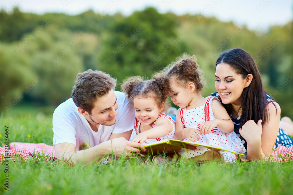 Young family reading a book outdoors lying on the grass in the p Young family reading a book outdoors lying on the grass in the p