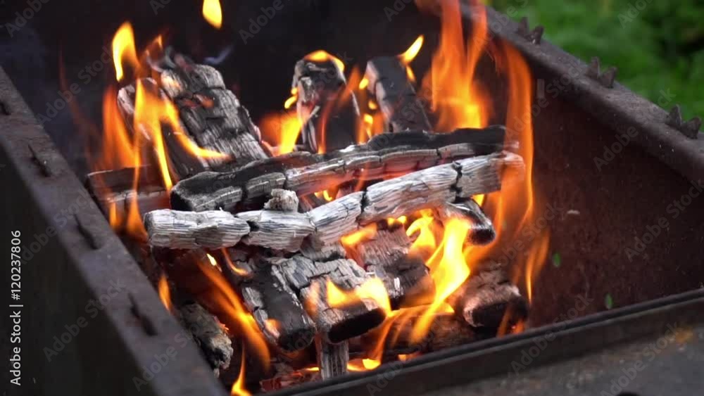 Burning flame at the metal square barbecue, closeup. Bonfire on picnic. Slow motion
