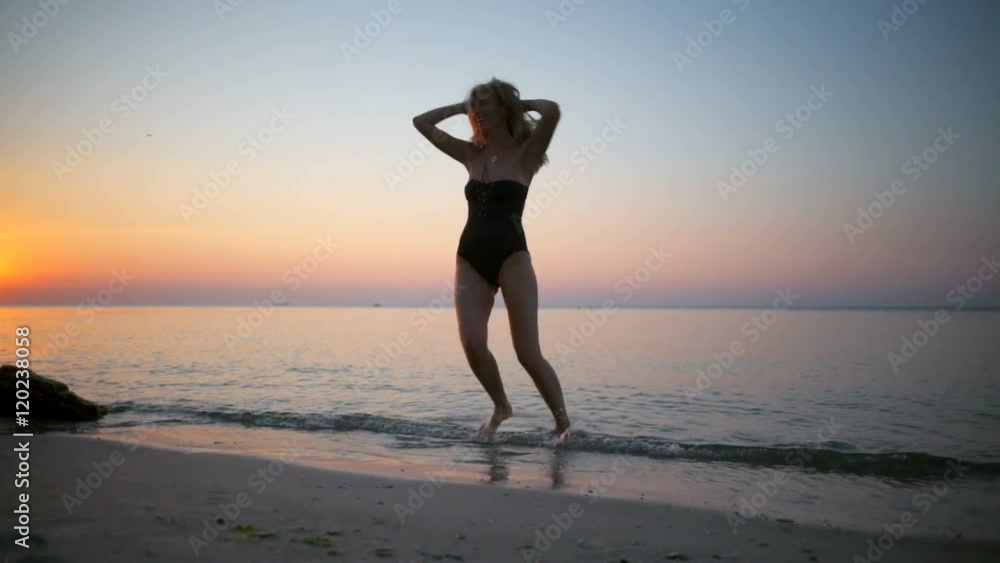 Young beautiful girl in swimwear smiling, whirling, walking at seaside