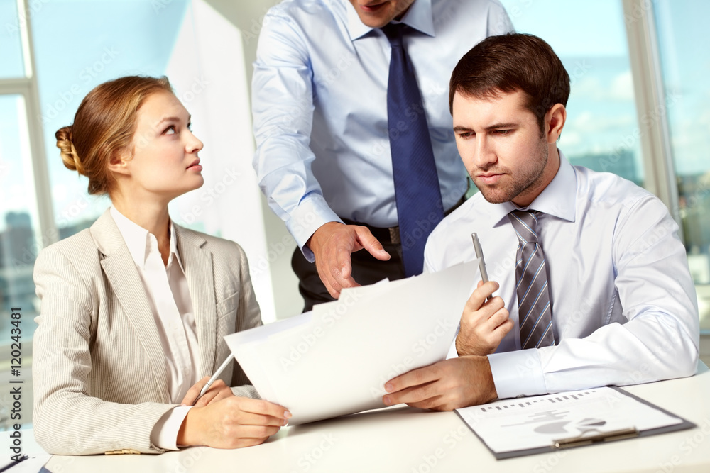 Business leader pointing at papers being discussed by his colleagues Business leader pointing at papers being discussed by his colleagues
