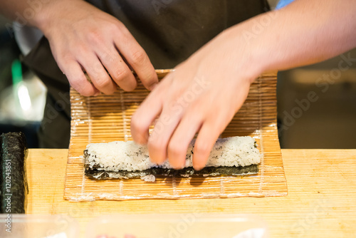 Chef rolling up sushi on a bamboo mat. 