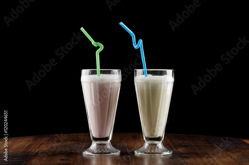 Milk shake (cocktail) with berry and banana in glass on brown wooden table