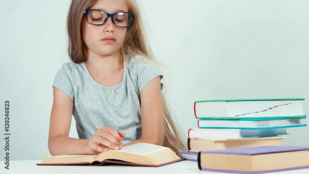 Schoolgirl lying on the stack of books wakes up and saddly reading textbook Schoolgirl lying on the stack of books wakes up and saddly reading textbook