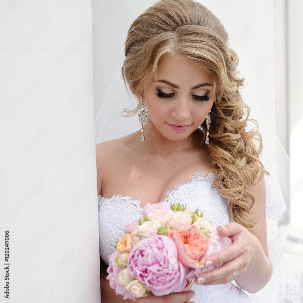 Beauty bride in bridal gown with bouquet and lace veil in the nature. Beautiful model girl in a white wedding dress. Female portrait in the park. Woman with hairstyle. Cute lady outdoors