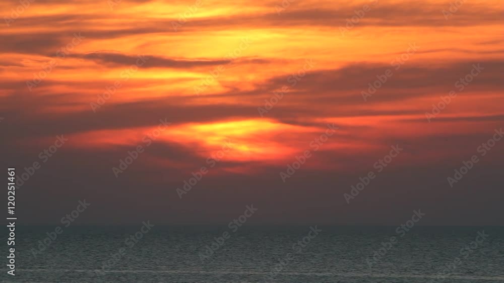 Sunset on a sea with sun hidden by clouds which cover the whole sky. It is windy and there are waves on the water surface. Also birds which cross the sky are visible. Sunset on a sea with sun hidden by clouds which cover the whole sky. It is windy and there are waves on the water surface. Also birds which cross the sky are visible.