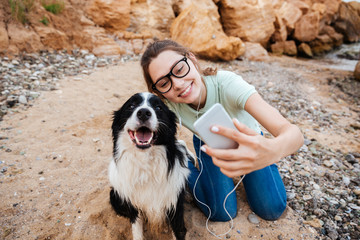 Girl in eyeglasses taking selfie with her dog on smartphone