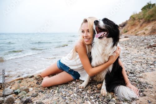 Smiling woman hugging her dog on the beach photo