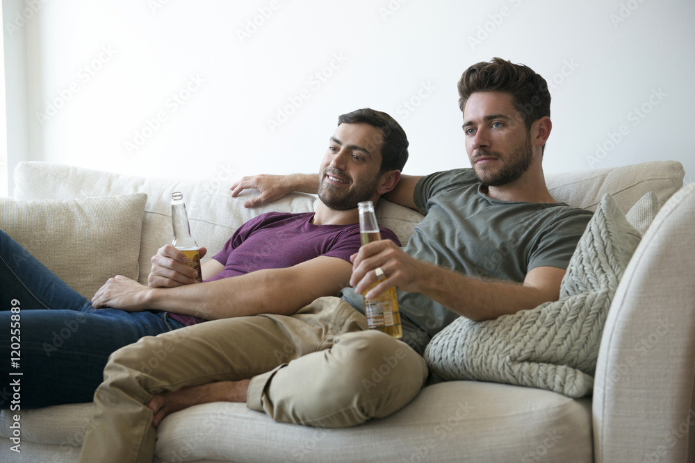 Gay Male Couple On Sofa At Home Watching Tv Drinking Beer Stock Photo