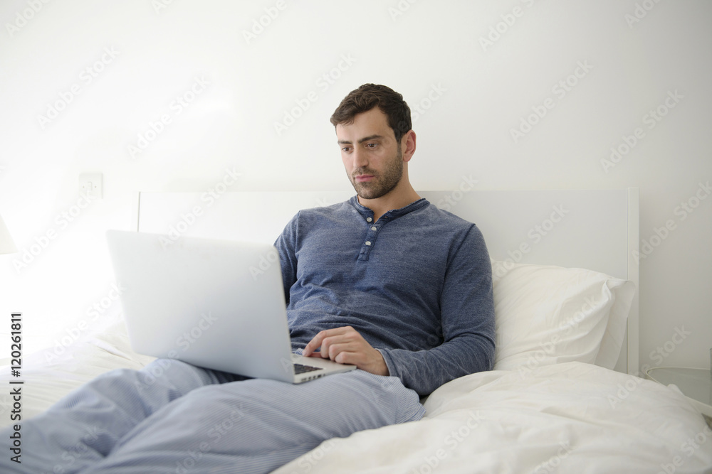 Man using a laptop while relaxing on the bed Man using a laptop while relaxing on the bed