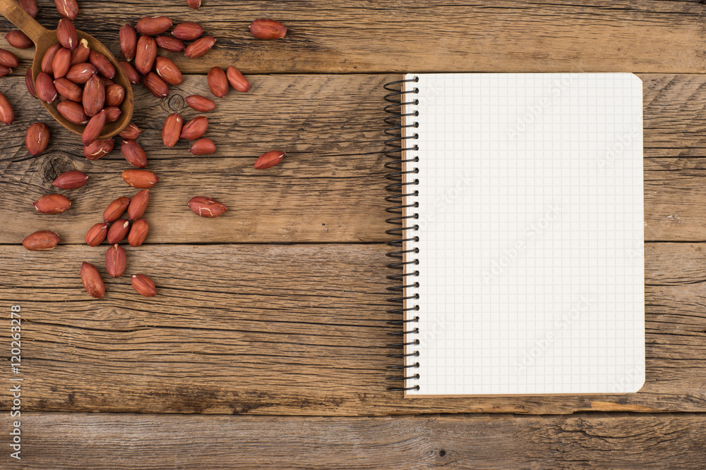 Peanuts in a spoon with a notebook on an old wooden table. Peanuts in a spoon with a notebook on an old wooden table.