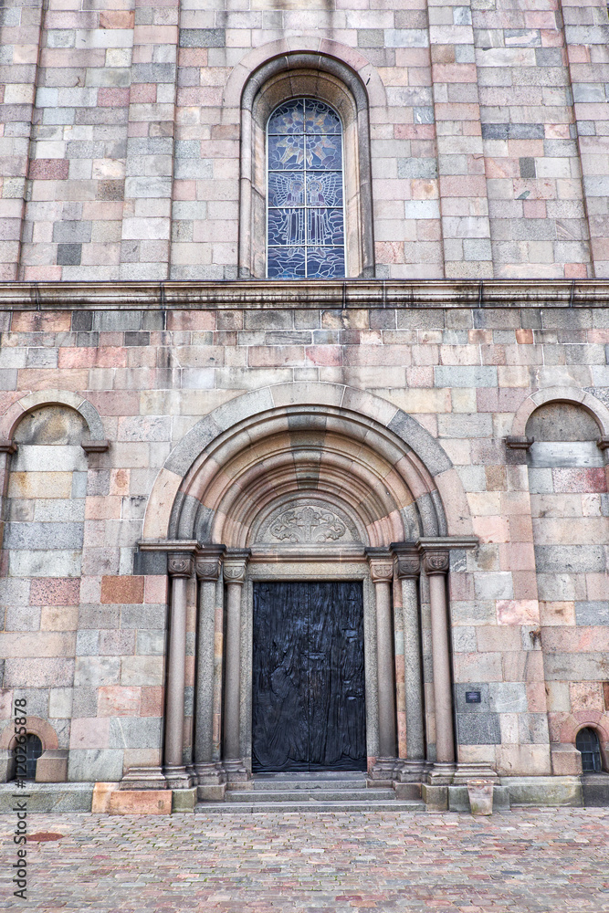 Fototapeta premium The entrance door and a leaded window, in Viborg Cathedral, build of ashlar granite, sandstone and red stone from the island Fur
