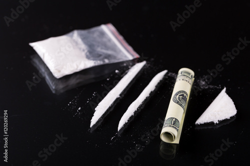 Rolled hundred dollars banknote, two lines and pile of cocaine on black background, closeup  photo