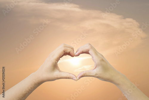 Closeup heart shape by two woman hand on evening sky with sunset background