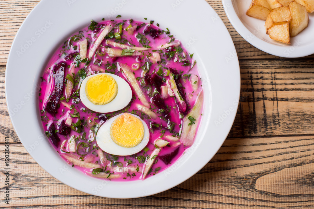 Close-up of cold beetroot soup with cabbage and egg served with fried potatoes on a white plates at the rustic wooden background Close-up of cold beetroot soup with cabbage and egg served with fried potatoes on a white plates at the rustic wooden background