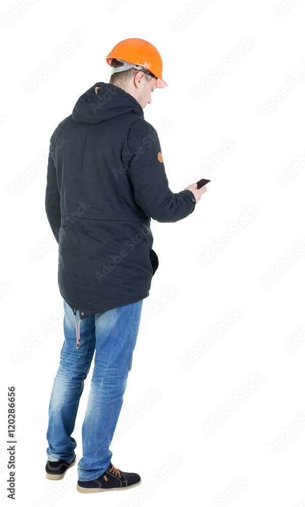 Backview of an engineer in construction helmet stands and using a mobile phone. Standing young guy. Rear view people collection. backside view of person. Isolated over white background. Backview of an engineer in construction helmet stands and using a mobile phone. Standing young guy. Rear view people collection. backside view of person. Isolated over white background.