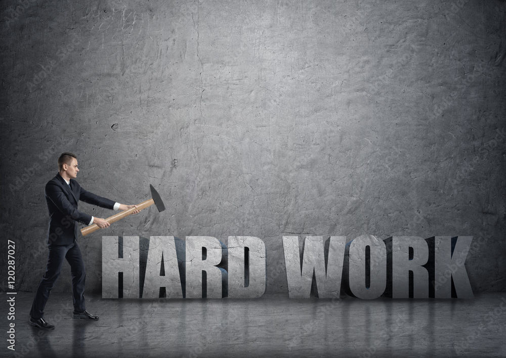 Obraz premium Side view of young businessman crashing 3D concrete 'hard work' words with a hammer