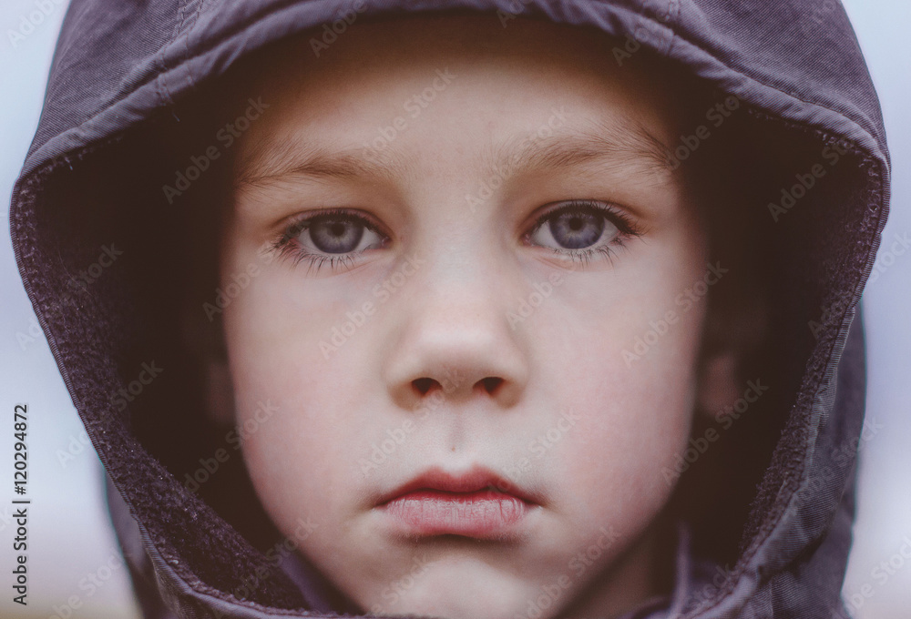 sad boy in a black hood. closeup. kid with big blue eyes and long lashes sadly looking at the camera outdoors sad boy in a black hood. closeup. kid with big blue eyes and long lashes sadly looking at the camera outdoors